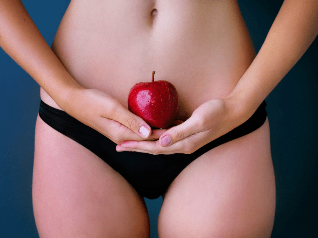 mujer sosteniendo una manzana a la altura de su útero